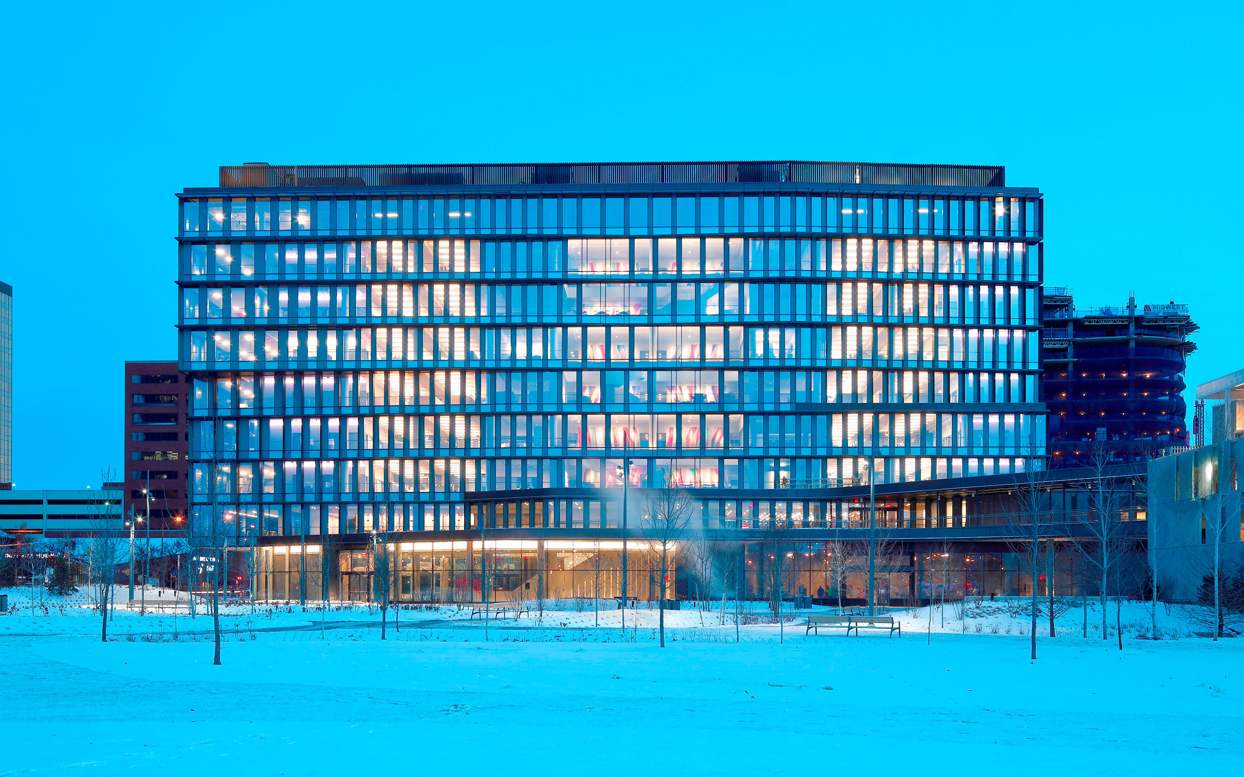 Cummins facade at dawn in winter with snowy landscaping and light pouring from windows.