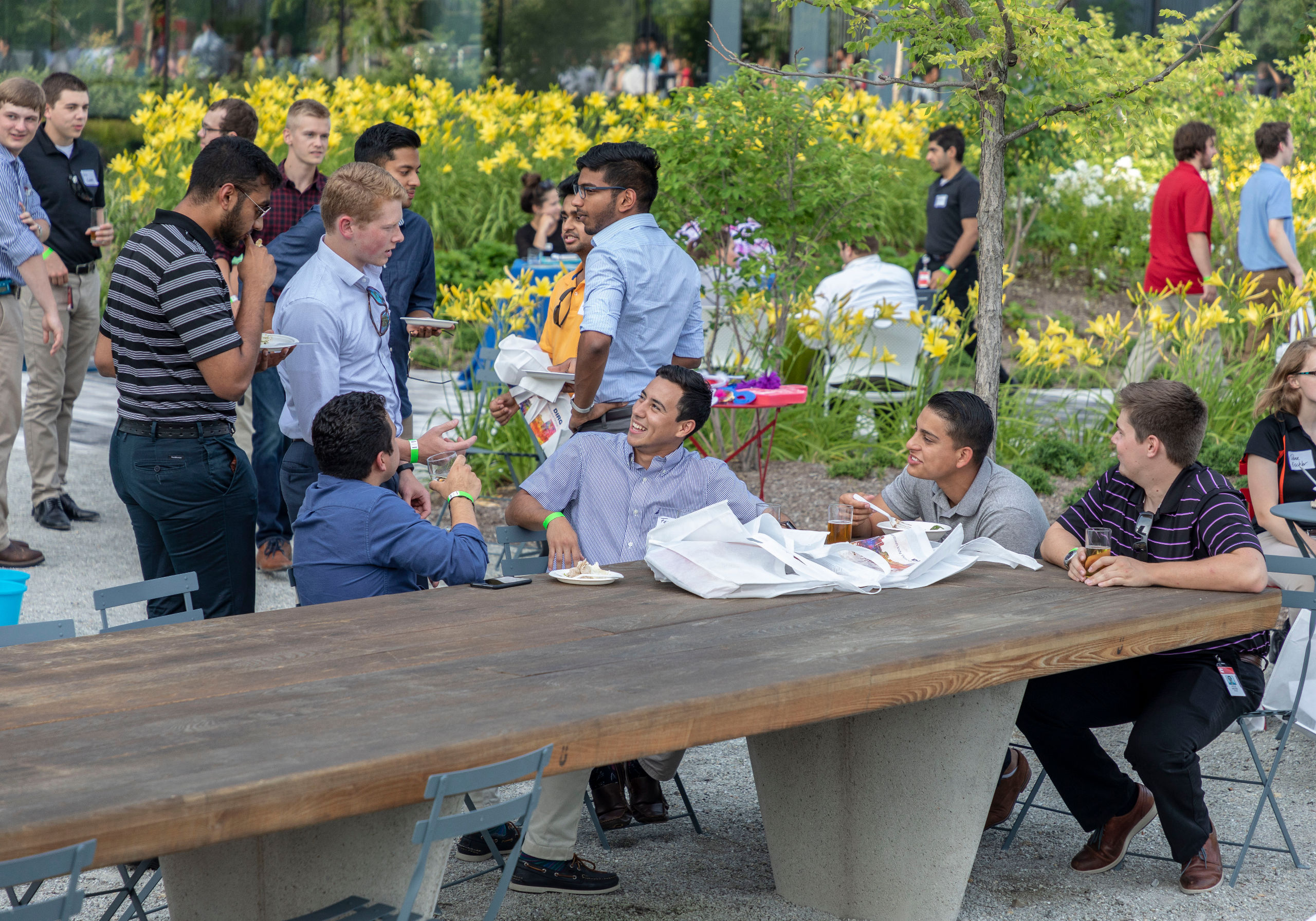 Group of young men sitting at outdoor table eating and drinking.