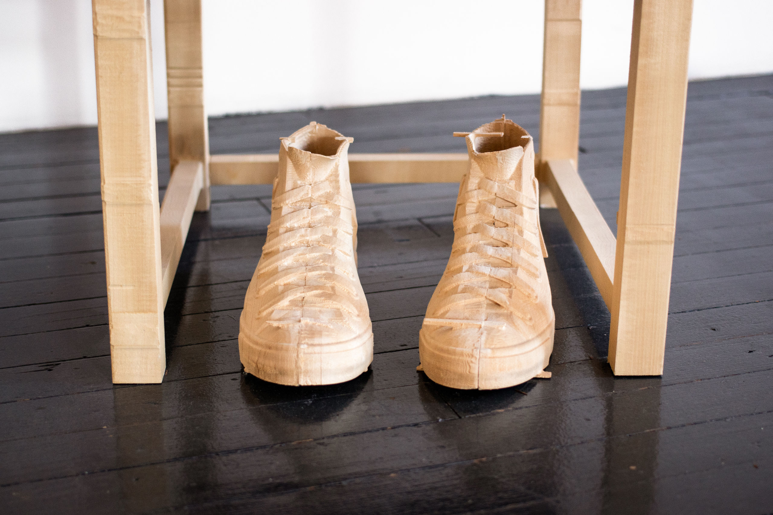 Wood sculpture of empty sneakers in front of a chair.